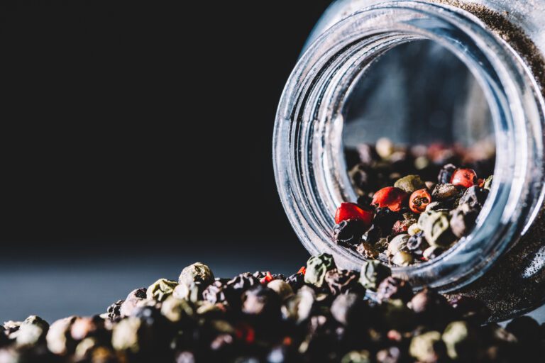 Mixed peppercorns spilling from a glass jar